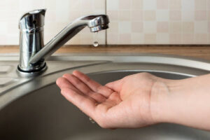 A hand cupped beneath a leaky faucet to catch a water droplet.