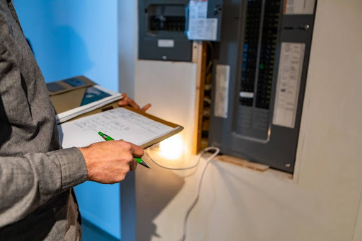 A man inspecting a home's electrical panel; he's holding a clipboard and pen.